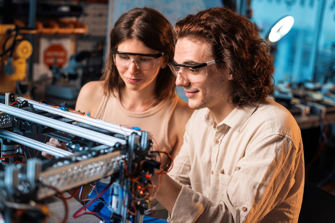Studentka i student w okularach ochronnych budują robota w laboratorium