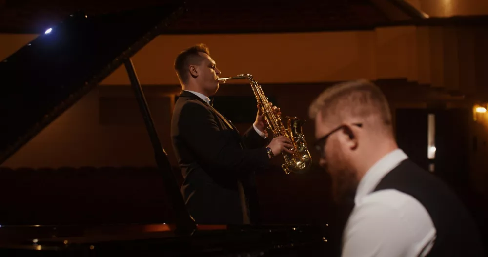 Muzycy jazzowi z saksofonem grają na scenie w przyciemnionej sali.